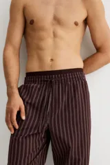 Pantalón de popelina color bordó con finas rayas verticales blancas. Presenta cintura elástica con cordón ajustable y bolsillos laterales. Corte relajado.