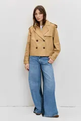 Cazadora corta de estilo gabardina en color tostado, con diseño cruzado de doble botonadura, solapas amplias, mangas largas con trabillas en los puños y hombreras.
