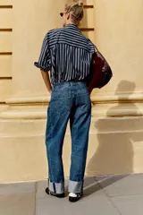 Jeans baggy de tiro medio con pernera holgada, diseño de cinco bolsillos y bajo acabado en vuelta. Cuenta con cintura elástica en la espalda y cierre frontal con cremallera y botón.