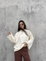 Buzo oversize de color crudo con diseño de costuras expuestas en contraste y terminaciones desflecadas en mangas y ruedo. Presenta un corte holgado con mangas anchas.