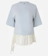 Remera overboxy de algodón color celeste, con cuello redondo, mangas cortas amplias y bajo asimétrico con aplicación de encaje blanco.