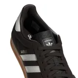 Championes Adidas Gazelle Indoor, modelo de corte clásico y retro fabricado en gamuza de color marrón oscuro, con las tres franjas características de la marca y la lengüeta del talón en color blanco. Incluye la inscripción "GAZELLE" en letras doradas en el lateral y suela de caucho translúcido tipo caramelo.