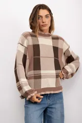 Sweater de punto con diseño de cuadros escoceses en tonos marrones y beige. Presenta un corte oversize, cuello redondo y terminaciones con volados en el cuello y los puños.