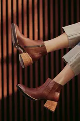 Botín de cuero negro, caña corta, con punta cuadrada y cierre lateral. Presenta un tacón de madera de altura media y detalles en charol con textura de cocodrilo en el talón.