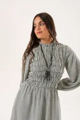 Vestido largo a rayas verticales en tonos verde y blanco, con cuello alto fruncido, mangas largas abullonadas y falda amplia. Presenta un diseño de nido de abeja con hilo elástico hasta la cintura.