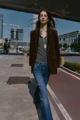 Blazer de piel 100% color marrón oscuro, con cuello solapa, manga larga con hombreras y bolsillos delanteros con solapa. Presenta pespuntes decorativos en contraste y cierre frontal con un botón.