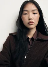 Jersey de punto grueso en color marrón chocolate, con diseño recto, cuello de solapa ancha y cierre frontal de cremallera. Presenta manga larga y un tejido de textura acanalada.