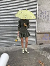 Vestido corto marrón con estampado floreado, confeccionado con tejido fruncido tipo nido de abeja en el torso y mangas largas con diseño abullonado y volados en los puños. Presenta cuello alto con volado y falda evasé corta con vuelo.