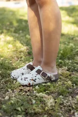 Zueco con capellada de pelo de vaca con manchas marrones y negras sobre base blanca, plantilla anatómica de cuero y hebilla lateral ajustable.