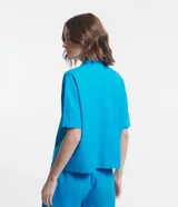 Camisa de manga corta confeccionada en mezcla de viscosa y lino color turquesa. Presenta cuello camisero con escote en V, bolsillos frontales de parche y cierre frontal con botones geométricos de efecto carey.