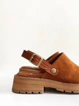 Zueco de cuero gamuzado color óxido, con tira trasera ajustable mediante hebilla metálica. Presenta una suela de plataforma con textura acanalada y detalle de textura reptil en la tira posterior.