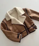 Chaqueta tipo gamulán de cuero sintético en color tostado, con interior y cuello de corderito sintético en color crema. Presenta cierre frontal cruzado, detalles de ribetes en cuero oscuro y correas ajustables con hebillas en los puños y laterales.