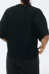 Remera de algodón negro, con cuello redondo ribeteado y mangas cortas de diseño murciélago y corte amplio.