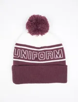 Gorro tejido con diseño de bloques de color en bordó y blanco, con vuelta en el borde inferior y pompón superior. Presenta la palabra 'UNIFORM' tejida en el frente.