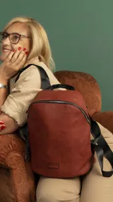 Mochila de símil cuero color negro, con asa de mano superior y correas regulables para llevar al hombro. Presenta cierre principal curvo en la parte superior y un bolsillo oculto en la espalda. Incluye llaveros colgantes decorativos en el tirador del cierre principal.