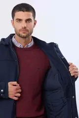 Saco de paño azul marino con capucha desmontable, cierre frontal oculto por cartera y bolsillos laterales. Presenta diseño de abrigo con detalles en los puños.