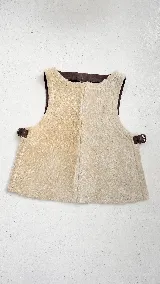 Chaleco de corte oversize confeccionado en material tipo corderito color beige, con detalles de ribetes y hebillas ajustables en los laterales en color marrón oscuro.