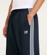Pantalón deportivo de corte recto y holgado, color negro con rayas blancas laterales. Cuenta con cintura elástica con cordón ajustable, bolsillos laterales y detalle de costura vertical frontal.