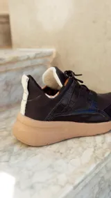 Championes deportivos de cuero en tonos marrón, tostado y marrón oscuro, con detalles de estampado animal print de leopardo en el lateral, suela gruesa blanca y cordones elásticos.