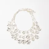 Collar de tres niveles con cadena fina plateada y múltiples dijes circulares de superficie irregular y texturizada.