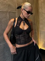 Top negro de encaje con diseño estilo corset, cuello alto con abertura y lazo decorativo para atar al frente.