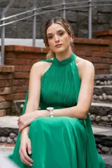 Vestido largo de gasa color verde, con cuello alto drapeado y un diseño fluido con lazos laterales.