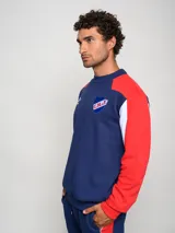 Buzo de felpa con diseño de bloques de color, predominantemente rojo en el cuerpo y azul marino en las mangas y hombros. Presenta el escudo del Club Nacional de Football y el logo de Umbro en el pecho.