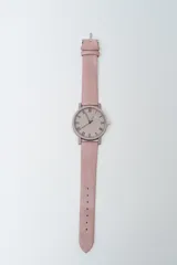Reloj analógico con correa de cuero sintético color rosado pálido y caja a juego. La esfera es beige claro con números romanos en negro.