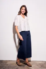 Blusa de viscosa color marrón, con escote en V, mangas cortas abullonadas y cierre frontal con botones. Cuenta con pequeños detalles bordados distribuidos por la prenda.