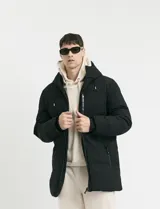 Campera puffer de corte largo, color verde militar, con capucha fija, cierre frontal y puños elásticos internos.
