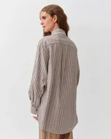Camisa de corte recto y silueta fluida, con estampado a rayas marrones y blancas. Presenta cuello clásico, cierre frontal con botones y un bolsillo aplicado en el pecho. Las mangas largas son ligeramente abullonadas, con puños ajustados que aportan volumen a la prenda.