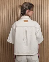 Sobrecamisa de denim soft color beige, con cuello camisero, mangas cortas amplias, bolsillos frontales con solapa y cierre de botones metálicos.