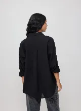 Camisa negra de manga larga con cierre frontal de botones, cuello camisero y bolsillo en el pecho con pequeño parche bordado de la marca. Corte holgado y relajado.