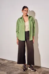 Camisa de corte oversize con estampado de rayas verticales en tonos verde, blanco y ocre. Presenta cuello clásico, cierre frontal con botones, bolsillo en el pecho y mangas largas con puños abotonados.