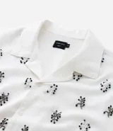 Camisa de manga corta para hombre, corte boxy, color blanco con cuello bowling y un estampado repetitivo de figuras geométricas negras.