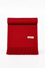 Bufanda de tejido suave en color tostado, con flecos en los extremos y una pequeña placa metálica dorada grabada con el logotipo de la marca.