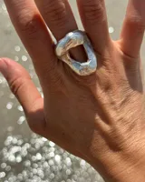 Anillo plateado con forma orgánica irregular y un agujero en el centro.