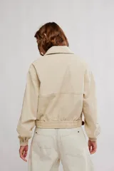 Campera bomber de sarga color beige, de calce amplio, con cuello con solapa, cierre frontal a cremallera, bolsillos al frente y puños y cintura elastizados.