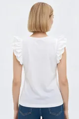 Remera de algodón color blanco, de corte al cuerpo, con cuello redondo y detalles de volados en las sisas.