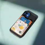 Billetera tarjetero con estampado de flores de colores y borde superior de cuero marrón.