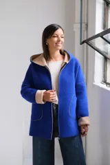 Tapado de paño color azul con capucha, cierre frontal y detalles en color beige en el interior de la capucha, puños y bordes de los bolsillos.
