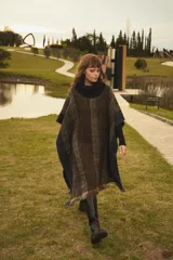 Poncho marrón con diseño de espiga en tonos beige y azul. Tiene cuello alto negro y flecos en el ruedo.