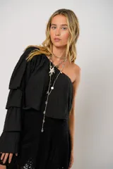 Blusa negra con un hombro descubierto y manga larga con volados.