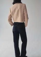 Chaqueta de tweed en color beige con diseño recto, cuello redondo y cierre frontal de doble botonadura con botones dorados. Presenta dos bolsillos de parche en el pecho y forro interior.