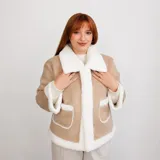 Campera tipo gamulán de color beige con forro y detalles de corderito sintético blanco en cuello, puños, bolsillos y ruedo. Presenta cierre frontal con botones y dos bolsillos frontales con solapa.