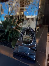 Bolso negro tipo hobo con tachas plateadas en el contorno y bolsillo frontal.