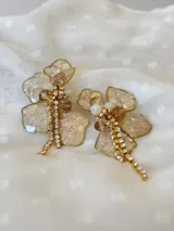 Aros colgantes con forma de flor, pétalos de resina color champagne con borde dorado, centro con cuentas de cristal color ámbar y blanco, y flecos de strass dorados.