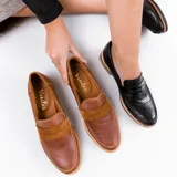 Mocasín de cuero vacuno negro con textura grabada tipo reptil. Presenta un diseño clásico con antifaz en el empeine, suela de goma en tono natural y taco bajo de madera.