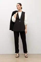 Chaleco largo sastrero de color negro, con escote en V profundo, cierre frontal con un botón metálico y bolsillos laterales con solapa.