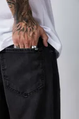 Jean de corte mom oversize, color negro lavado, con diseño de cinco bolsillos y cierre frontal con botón y cremallera.